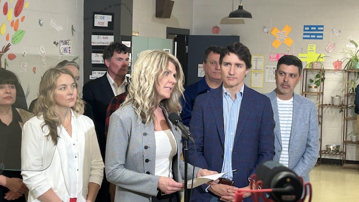 Une femme parle au micro, Justin Trudeau derrière elle.