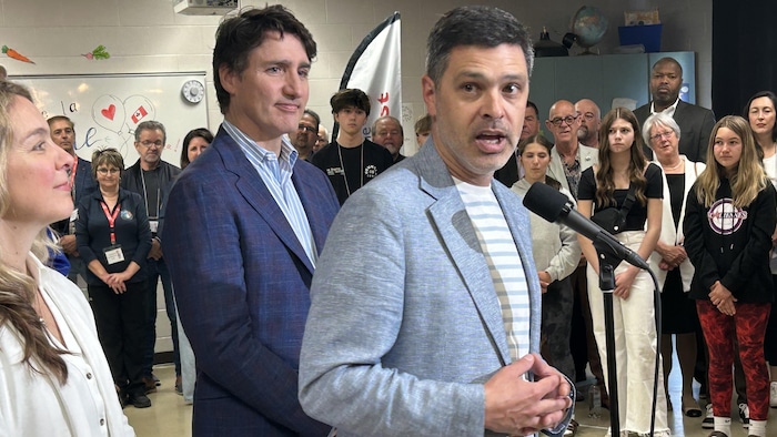 Serge Cormier debout devant un micro, Justin Trudeau derrière lui.