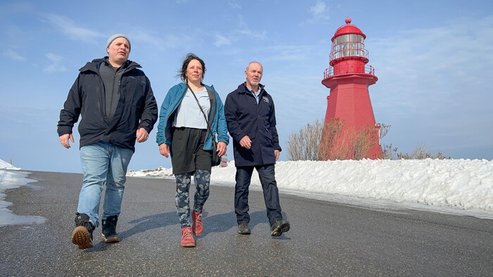 Trois personnes marchent devant le phare de La Martre.