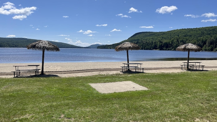 Une plage de sable fin sur le bord d'un lac. Des tables à pique-nique et des parasols sont disposés tout le long de la plage.