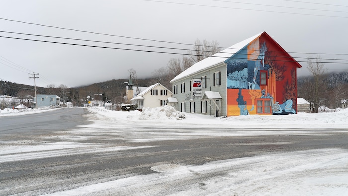 Bâtiment de deux étages situé sur la rue principale en hiver. Une fresque a été peinte sur la totalité de la façade de côté.