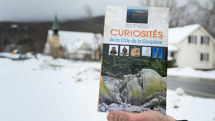 Le livre tenu dans une main. Un village flou se trouve en arrière-plan.
