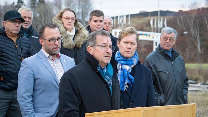 Le chef du Bloc se tient devant un lutrin alors que les deux se trouvent derrière lui.