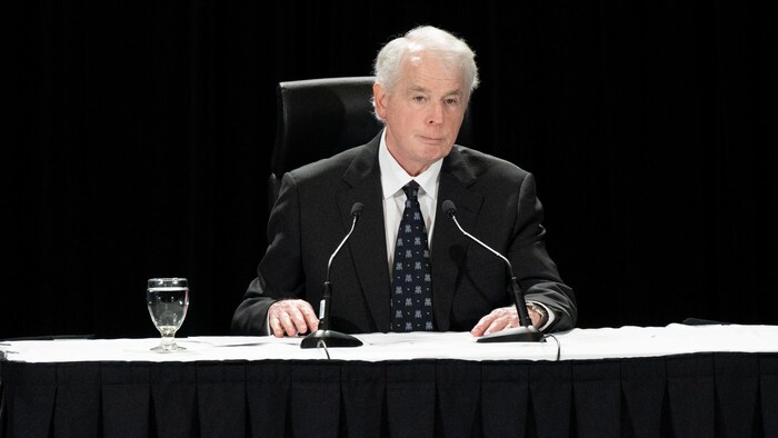 Paul Rouleau assis en conférence de presse.