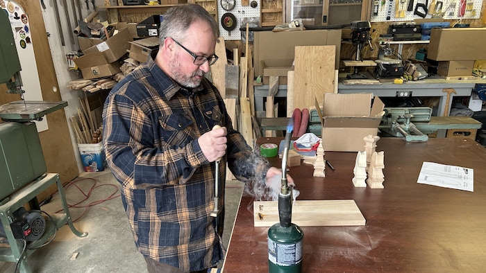 Pierre-Luc Gauthier utilise un outil chauffant sur un morceau de bois dans son atelier.