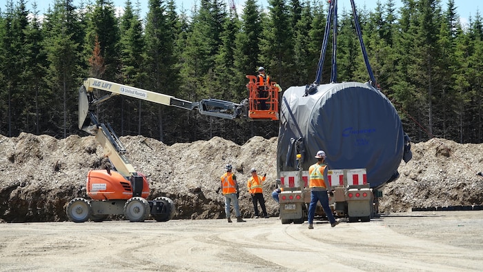 Des employés s'activent autour d'une pièce d'éolienne sur un chantier.