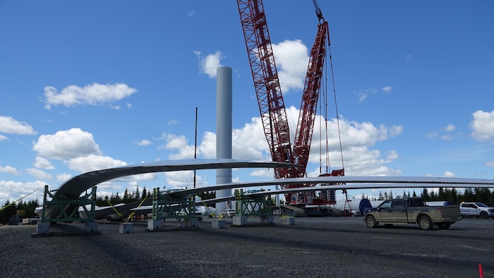 Des pales d'éolienne au sol avec une tour en construction à l'arrière.