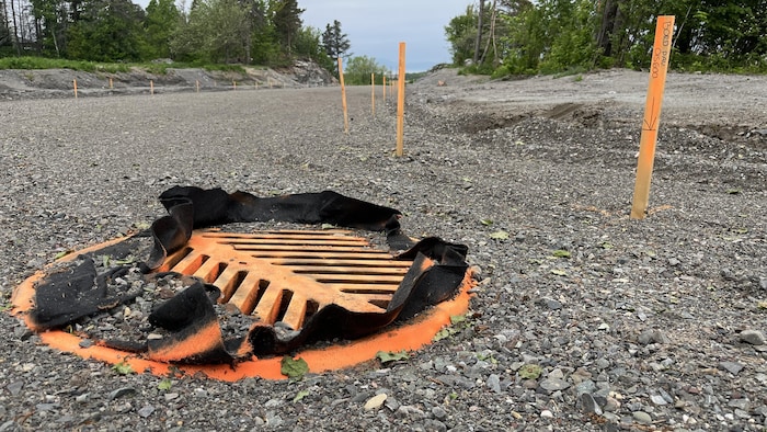 Grille d'égout sur le tracé d'une nouvelle rue en gravier bordée de piquets d'arpenteurs. 