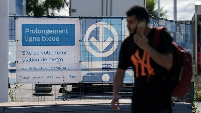 Un homme passe devant un panneau qui indique les travaux de prolongation de la ligne bleue du métro de Montréal.