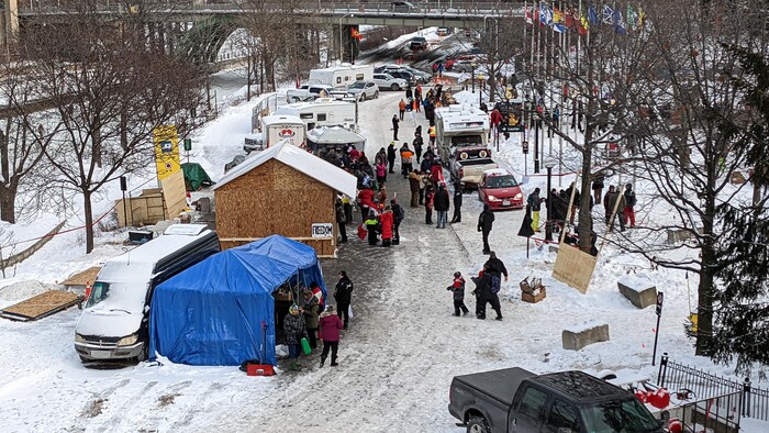 Des structures sont établies dans un parc et des véhicules y sont stationnés parmi des personnes.