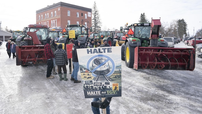 Une pancarte «Halte au TGV» tenue par un manifestant devant un groupe de personnes et des tracteurs agricoles.