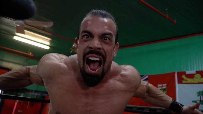 Un lutteur dans un ring crie en regardant l'objectif de la caméra.