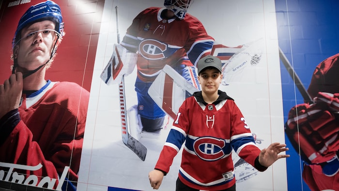 Un jeune garçon habillé aux couleurs du Canadien pose devant une image d'un gardien.