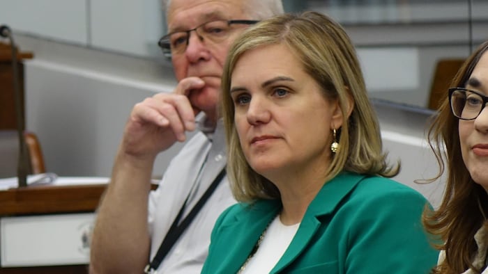 Une femme de profil, assise à l'Assemblée législative, écoutant ce qui se passe.
