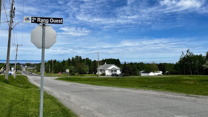 Un chemin adjacent à une route numérotée. Église de Trois-Pistoles et fleuve au loin.