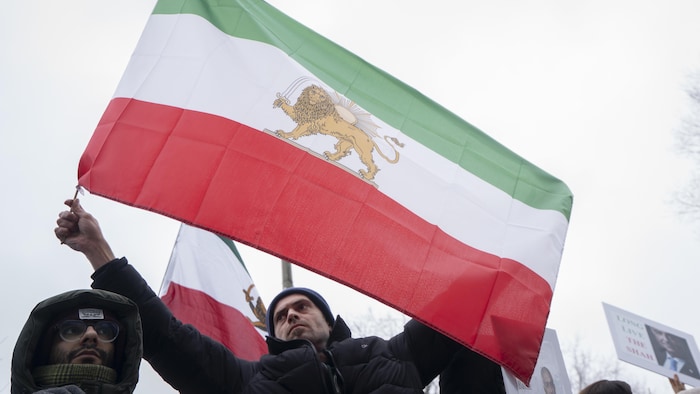 Deux hommes manifestent et l'un d'eux tient un drapeau arborant un lion brandissant un sabre devant un soleil.