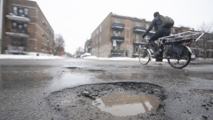 Un vélo passe à coté d'un nid-de-poule en plein hiver.