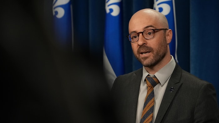 Un homme devant des drapeaux du Québec parle.