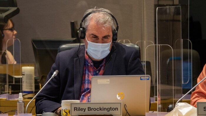 Une personne portant un masque, assise à un bureau, derrière un ordinateur.