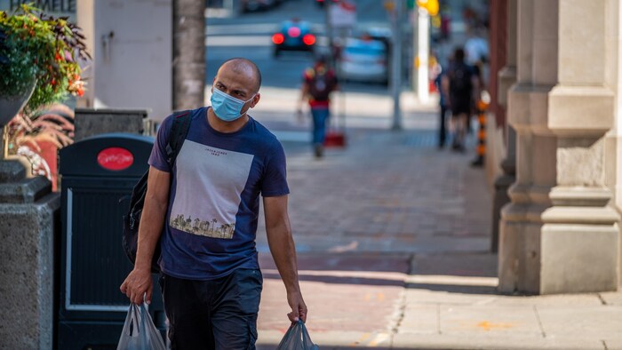 Un homme portant le masque marche avec ses sacs d'épicerie à Ottawa.