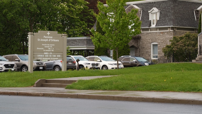 Un parc de stationnement avec un panneau affichant les horaires des messes devant.