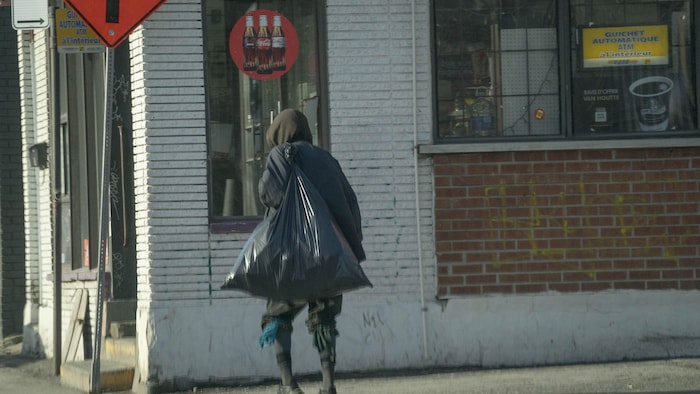 Un homme transporte un sac poubelle sur son dos dans une rue d'Hochelaga, à Montréal, le 6 mars 2024. 