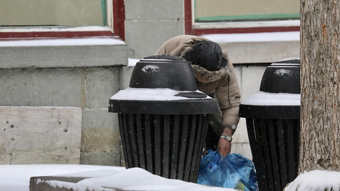 Un homme cherche des canettes vides dans une poubelle.