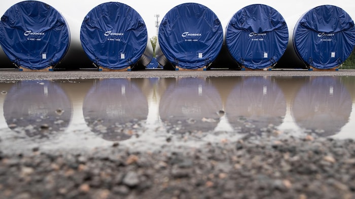 Des segments de mâts d'éoliennes devant une flaque d'eau.