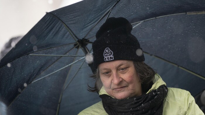 Portrait de Lisa Courtemanche, qui porte une tuque de la CSN, sous un parapluie.