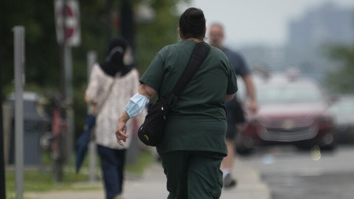 Une femme marche dans la rue, un masque médical attaché à son coude.