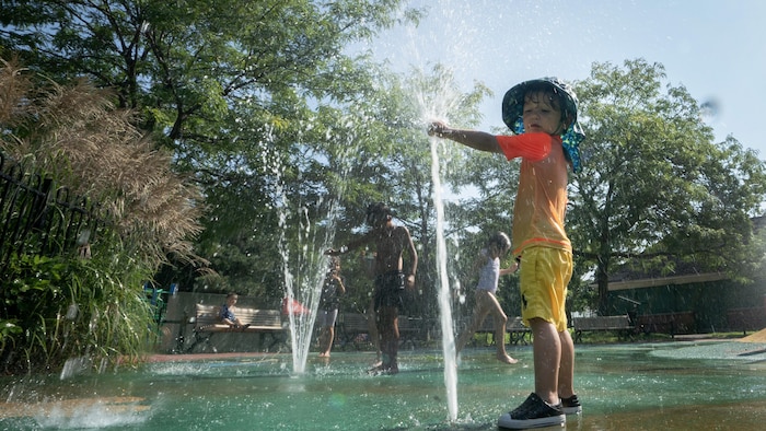 Deux enfants jouent dans l'eau dans un parc pendant une vague de chaleur.