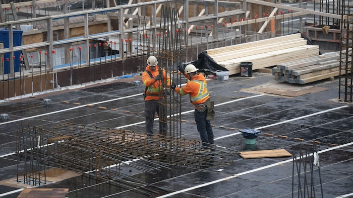 Deux travailleurs manipulent des matériaux sur un chantier. 