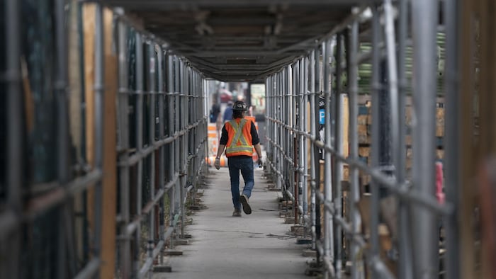 Un travailleur de la construction marchant sur un trottoir sécurisé.