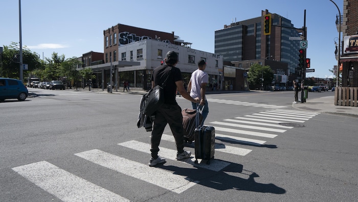 Deux hommes traversent la rue avec leurs valises.