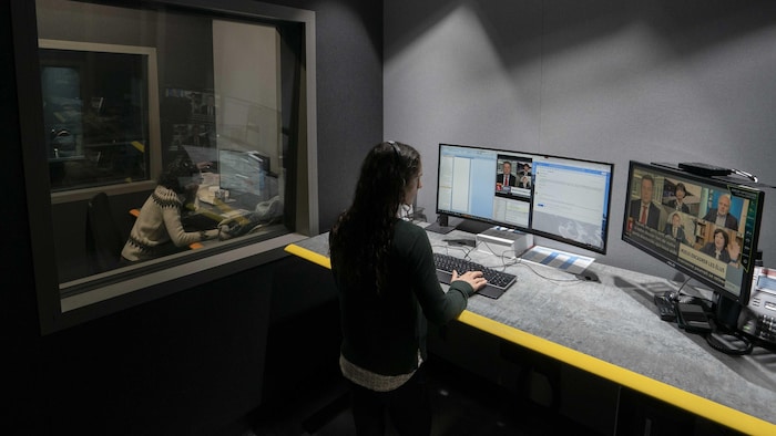 Deux sous-titreures travaillent dans leur studio respectif devant des écrans d'ordinateurs et de télévision.