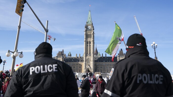 Des policiers d'Ottawa regardent les manifestants devant le parlement d'Ottawa.