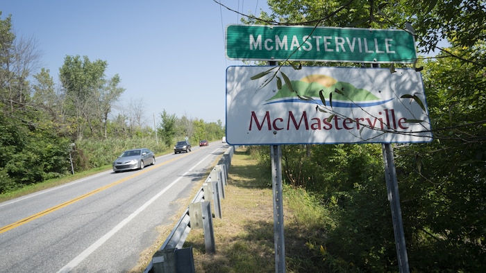 Pancarte illustrant McMasterville, en Montérégie, avec des voitures circulant sur une route.