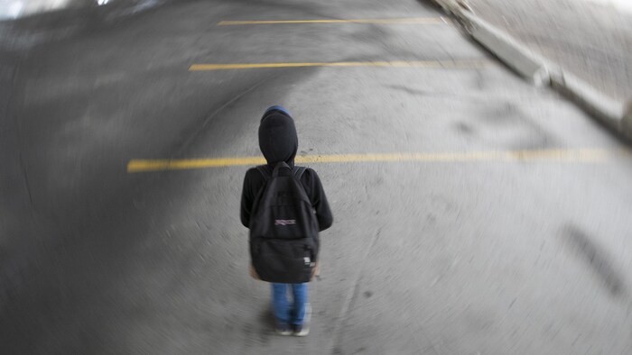 Un jeune porte un sac à dos dans un stationnement.