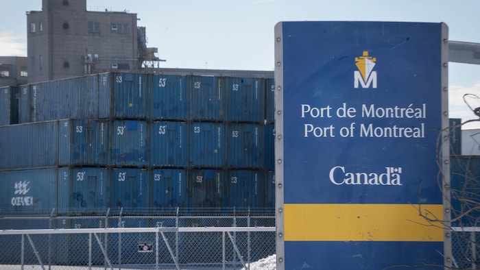 Une affiche du port de Montréal devant des conteneurs maritimes.