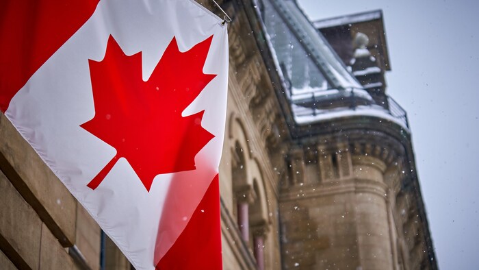 Un drapeau du Canada sous les flocons de neige, devant un édifice du parlement.