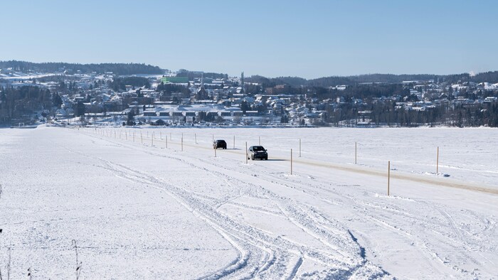 Deux autos circulent sur un chemin de glace qui relie les deux rives d'un lac. 