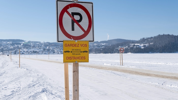 Une affiche interdiction de stationner et une affiche sommant les autos de garder une distance de 30 mètres entre elles, installée sur un chemin de glace sur un lac. 
