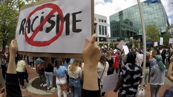 Un manifestant tient une affiche sur laquelle on voit un cercle rouge autour du mot "racisme".
