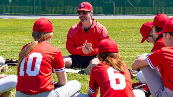 Jason Gagnon assit devant d'autres personnes sur un terrain de baseball.