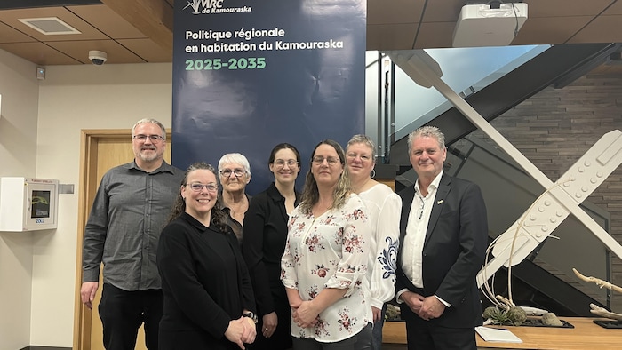 Un groupe de personnes posant devant une affiche. 