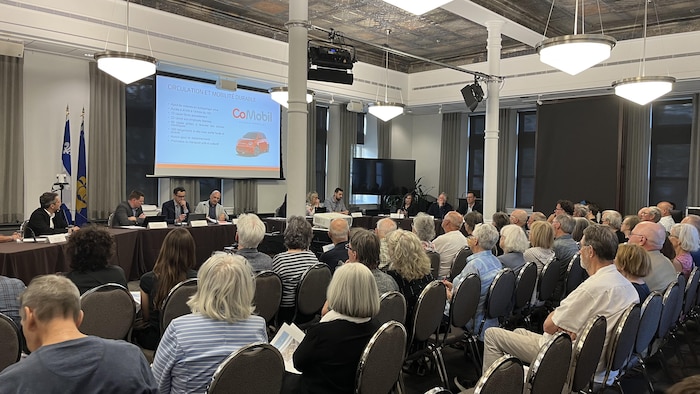 Des gens regardent une présentation sur un écran à l'avant d'une salle.