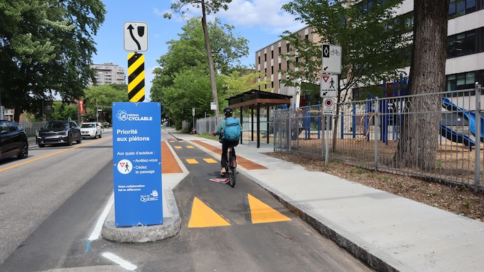 Une cycliste circule à vélo dans un corridor VivaCité en été.