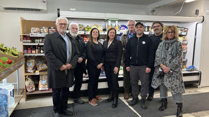 Un groupe de personnes réunies autour de la députée Amélie Donne devant un réfrigérateur rempli de fruits et de légumes. 