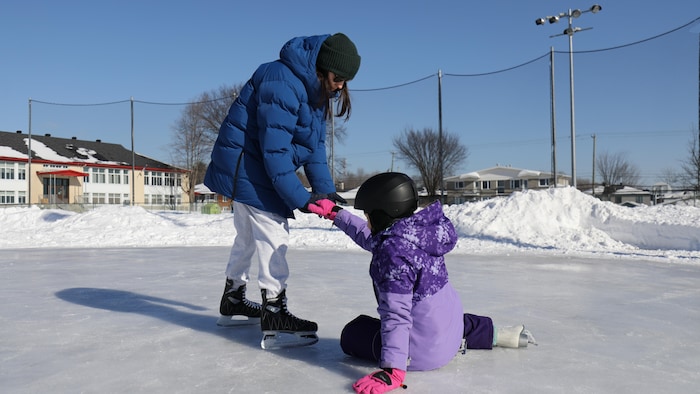 Une femme en patins aide une adolescente à se relever après qu'elle soit tombée sur la glace