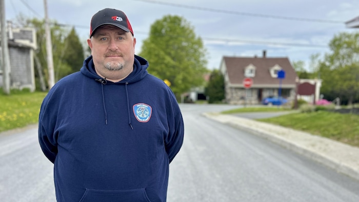 Un homme avec une casquette et un coton ouaté se tient debout dans une rue, les mains derrière le dos.
